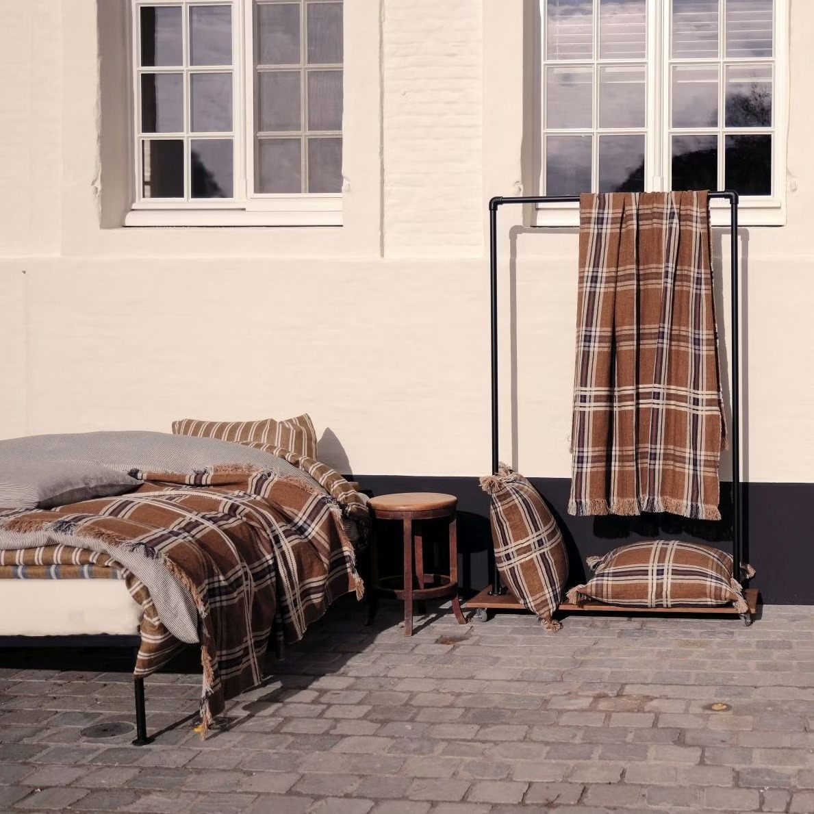 Brown check linen throw and cushions on a bed and rack in a sunny courtyard